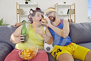 Funny man and fat woman having cheat day, sitting on sofa and eating unhealthy food