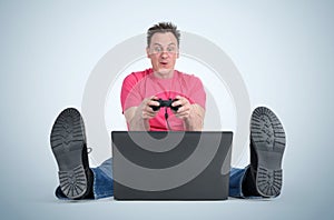 Funny man gamer sitting on the floor playing on laptop