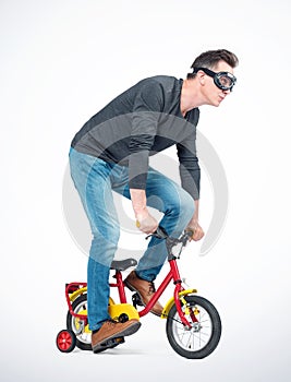 Funny man in goggles, jeans and black t-shirt pedals a children`s bicycle