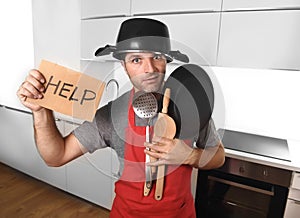 Funny man holding pan with pot on head in apron at kitchen asking for help
