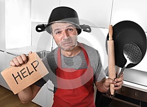 Funny man holding pan with pot on head in apron at kitchen asking for help