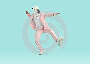 Funny man in horse mask and pink party suit dancing in studio with blue background