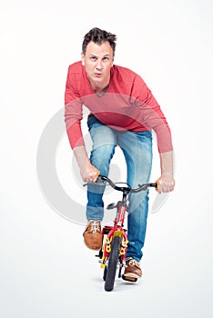 Funny man in jeans and a red T-shirt is rolling on a children`s bike. Front view.