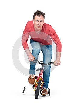 Funny man in jeans and a red T-shirt is rolling on a children`s bike. Front view. Isolated on white background.