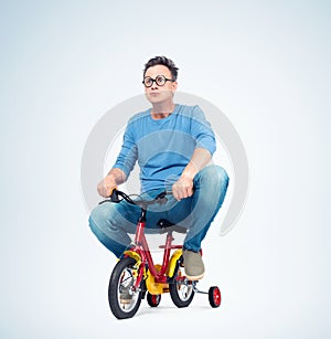 Funny man in jeans and t-shirt on a children`s bike, on light background.