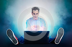 Funny man with joystick sits on the floor in front of a laptop. Gamer plays.