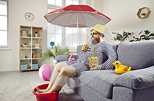 Funny man in living room at home imagines that he is resting on sea and sunbathing on beach.