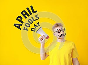 Funny man with megaphone on color background. April Fools' Day prank photo