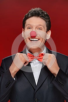 Funny man. Portrait of cheerful man with a clown nose touching h