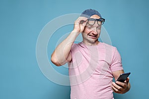 Funny man raised glasses to forehead and reads a message on a smartphone, with a strange expression on face. Copy space