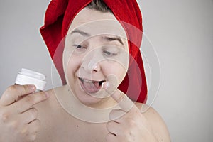 Funny man with a red towel on his head sniffs, tastes and smears a cream on his face. The concept of male self-care, spa