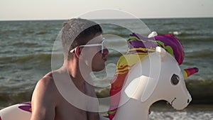 A funny man rides on an inflatable ring in the shape of a horse. Cheerful tourist on the sea beach. Summer vacation