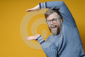 Funny man shows using some size, standing in an unusual pose and smiles joyfully while looking at the camera. Copy space