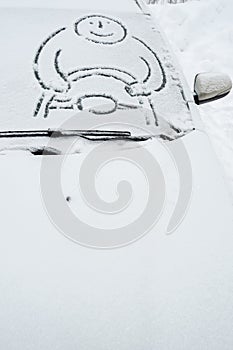 Funny man with a steering wheel is drawn on a snow-covered windshield, on a car on a frosty winter day. Copy space.