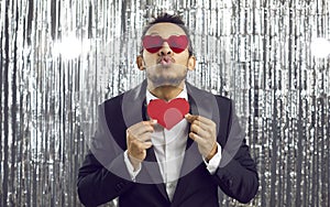 Funny man in suit and heart glasses holding Valentine card and pouting his lips for kiss