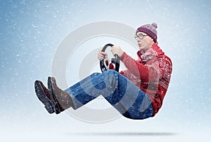 Funny man in sweater, scarf and hat, driving car with the steering wheel. Winter, snow, blizzard