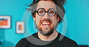 Funny man, unkempt, disheveled, wearing big black round glasses, smiling widely showing all teeth, holding