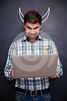 Funny man using laptop over blackboard background with drawn horns
