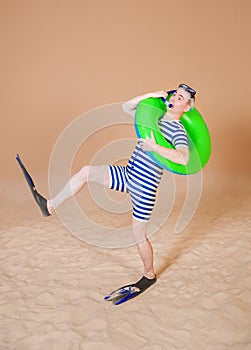 Funny man in vintage style striped swimsuit, inflatable ring, diving mask, snorkel and flippers walking on sand