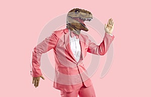 Funny man wearing pink suit and dinosaur mask dancing isolated on pink background