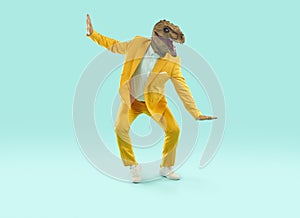 Funny man in a yellow party suit and a dinosaur mask dancing on a blue studio background