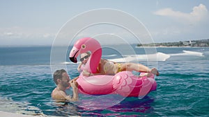 Funny married couple have fun, swim on pool party with pink flamingo