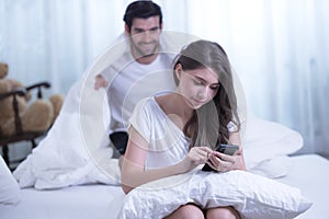 Funny married couple lying in bed and hiding under white blanket