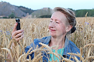 Funny mature woman doing selfie in gorgeous wheat field. 60 years old taking photos of herself