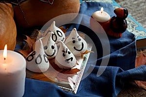 Funny meringue ghosts for Halloween party on autumn decorations. Golden leaves, pumpkin, blue textil and light of candles. Hallowe