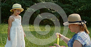 Funny mom and little daughter blow soap bubbles sitting on the lawn in the park