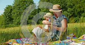 Funny mom and little daughter blow soap bubbles sitting on the lawn in the park
