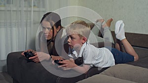 Funny mom with a small child playing video games together, they lie on the couch