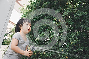 Funny moment of 3 Year old asian kid playing water with garden hose in backyard.