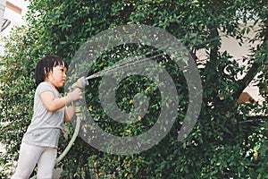 Funny moment of 3 Year old asian kid playing water with garden hose in backyard.