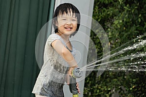 Funny moment of 3 Year old asian kid playing water with garden hose in backyard.