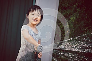 Funny moment of 3 Year old asian kid playing water with garden hose in backyard.