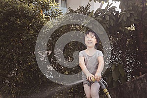 Funny moment of 3 Year old asian kid playing water with garden hose in backyard.