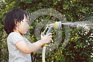 Funny moment of 3 Year old asian kid playing water with garden hose in backyard.
