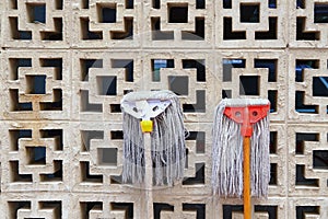 Funny mops heads against vent wall. Used wet floor mops drying on sun by lean on garage or warehouse air brick vent wall