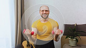 Funny muscular man smiles goofily, doing biceps exercises with dumbbells at home