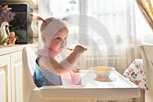 Funny naughty baby eating alone in the high chair