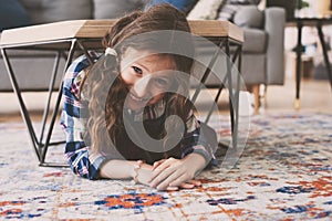 Funny naughty kid girl hiding under coffee table at home. Child playing