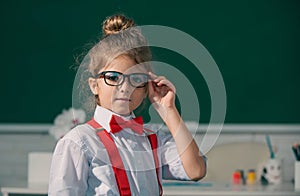 Funny nerd girl. Close-up portrait of merd girl in glasses in class room indoors. Little funny school girl face. Back to