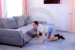 Funny nerd man is doing stretching exercise for back standing on all fours at home. Sport humor concept.