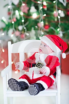 Funny newborn baby boy in Santa outfit under under Christmas tree