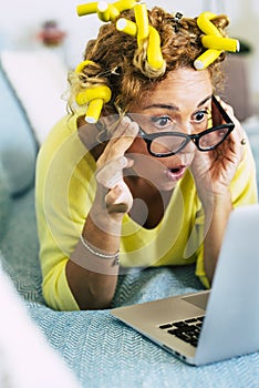 Funny and nice pretty woman surprised looking a laptop computer - yellow colors and curles foe home made getting ready hair style