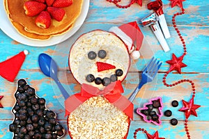 Funny oatmeal snowman with blueberry smile and strawberry nose. Festive idea for kids breakfast. New Year Christmas food top view