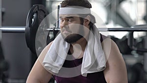 Funny obese man looks enviously at athlete people training in gym, insecurities