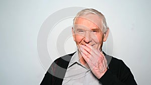 Funny old man laughs covering mouth with hand.