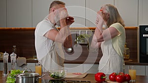 Funny old retired Caucasian couple make red paprika glasses peppers circles having fun happy middle-aged family woman